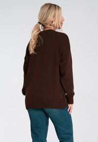 Brązowy sweter dzianinowy o luźnym kroju, z prążkowanymi mankietami i dołem. W połączeniu z niebieskimi dżinsami. Prosty design bez wyraźnych wzorów.