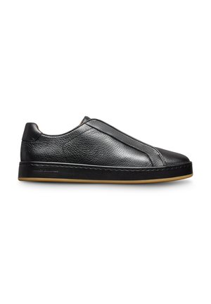 Chaussure noire en cuir à enfiler avec une texture lisse, des coutures discrètes et une semelle en caoutchouc brun clair. Design minimaliste sans marque visible.