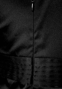 Tessuto nero con una superficie liscia presenta una zip nascosta e accenti di cuciture orizzontali in vita.