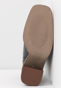 Chaussure noire texturée avec une semelle lisse marron, présentant un design strié pour l'adhérence. Les étiquettes indiquent "Fabriqué en Espagne" et la taille 37.