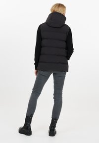 Sort polstret vest med høj krave, prydet med vandrette quiltede sektioner, kombineret med grå stramme jeans og sorte ankelstøvler.