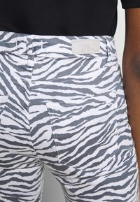 Primer plano de una persona que usa pantalones a rayas de cebra blancos y grises con bolsillos traseros y una etiqueta de marca LTB de color claro en la cinturilla.