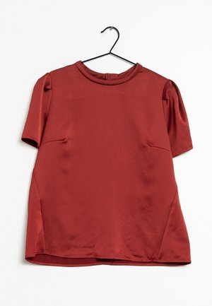 Roestroze blouse met korte mouwen, een ronde hals, licht opgeblazen schouders en een klein knoopsluiting op de achterkant, hangend aan een zwarte hanger.