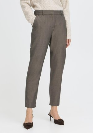 Femme portant un pantalon gris sur mesure longueur cheville, un pull en maille beige et des talons brun foncé à bout pointu avec des brides.