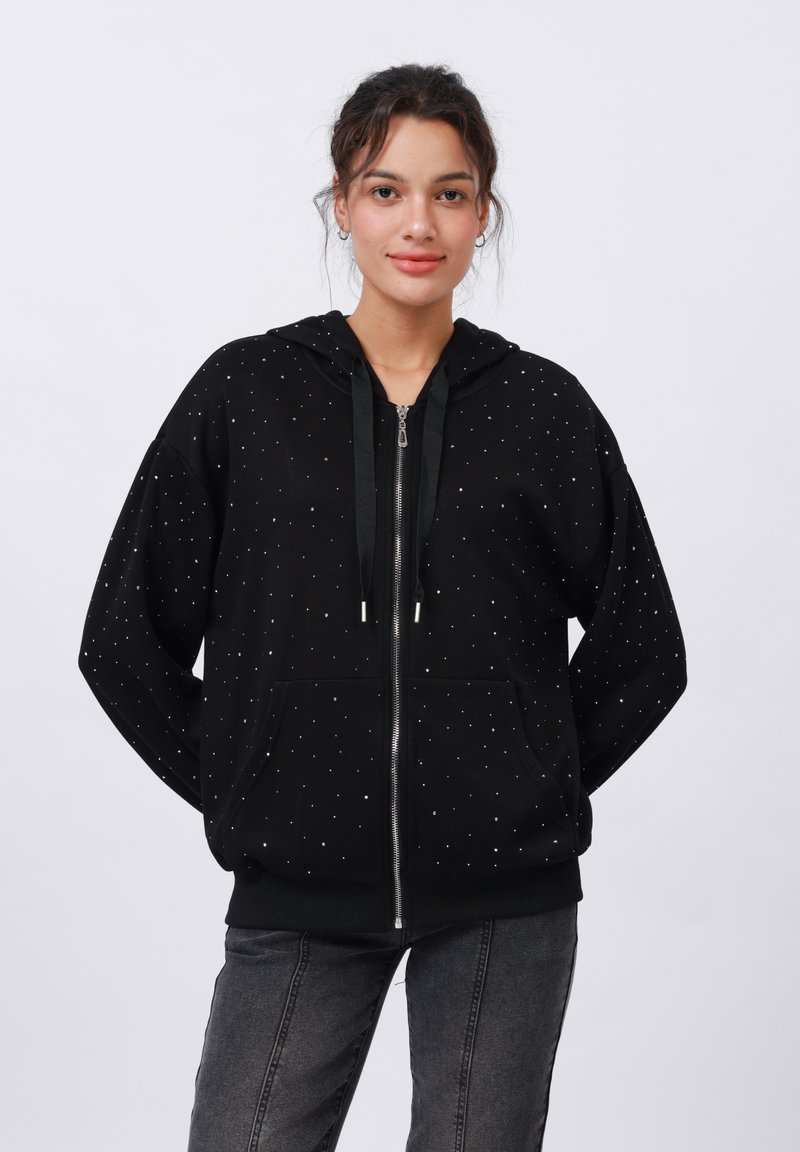 Melnās rāvējslēdzēju hoody izgatavota no mīkstas auduma, ar sudraba knopku izklājumu. Iekļauta ir kapuce ar aukliņu un priekšējās kabatas.