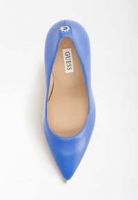 Chaussure à talons hauts en cuir bleu avec un bout pointu et un accent argenté à l'arrière. L'intérieur présente une doublure beige et une étiquette de marque.