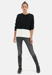 Zwart-wit gebreid sweater met ribbeltextuur, cropped ontwerp. Gecombineerd met grijze slim-fit jeans en donkere sport schoenen.