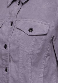 Lavendelfärgad kord skjorta med svarta knappar, två bröstfickor och sömnadsdetaljer. Tyget har ett mjukt, texturerat utseende.