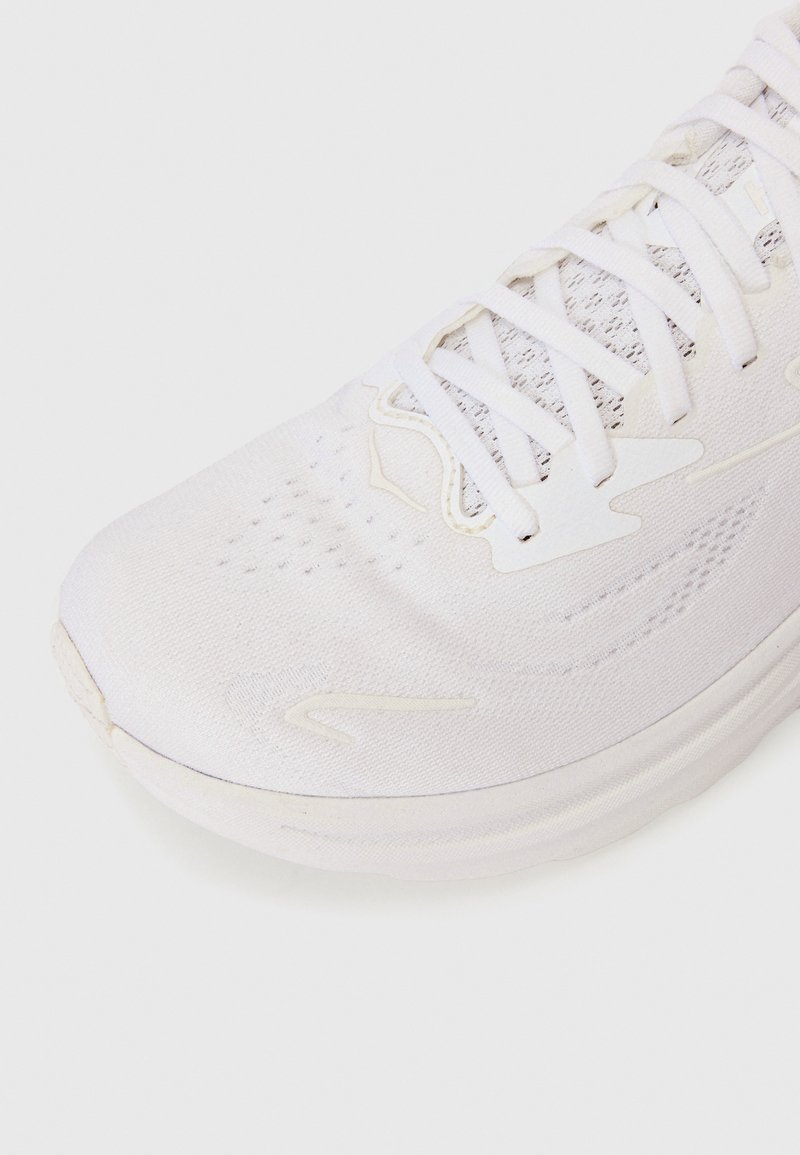 White athletic shoe with a textured upper, thin laces, and a smooth rubber sole. Features perforations for breathability and minimalistic design accents.