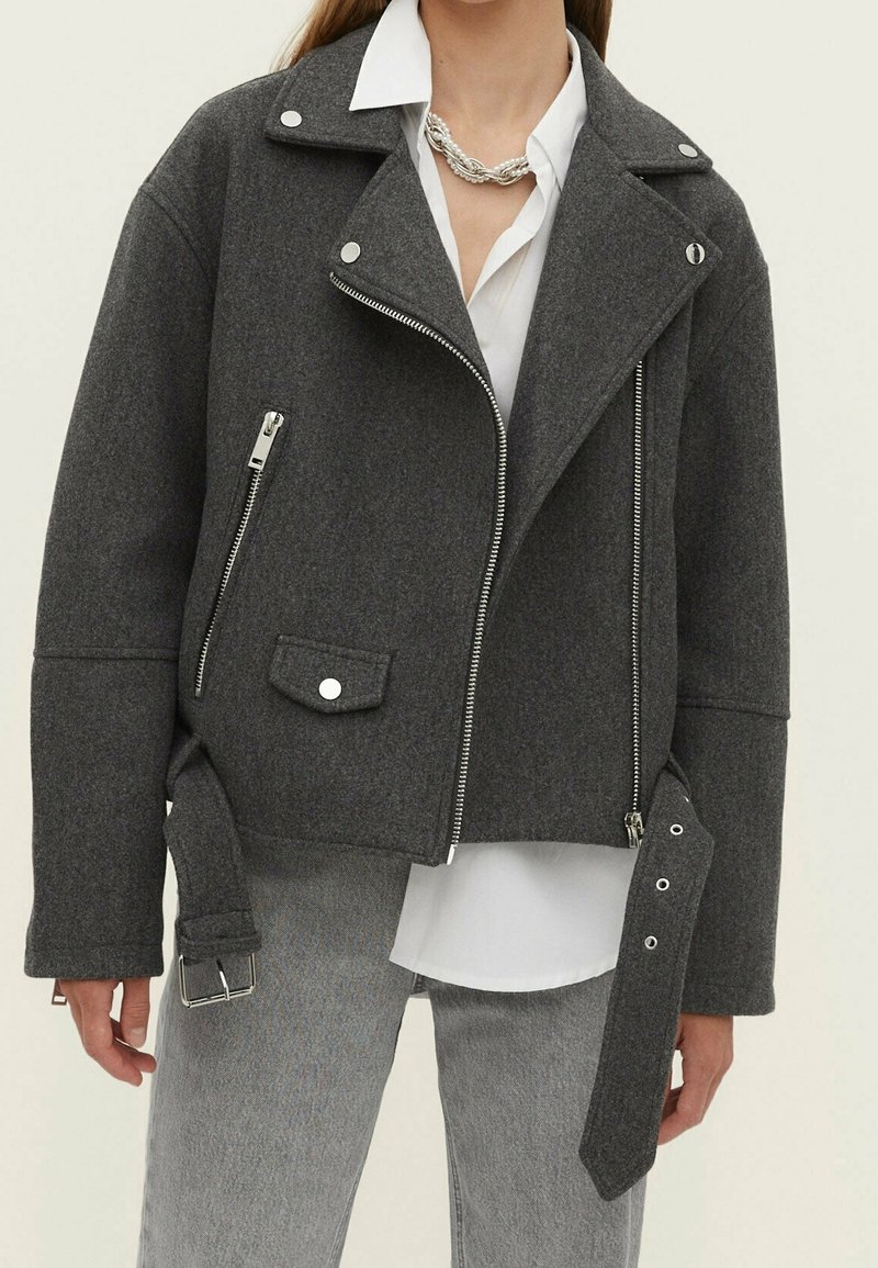 Veste de moto grise courte en mélange de laine texturée, avec quincaillerie argentée, poche latérale zippée et détail de sangle avec boucle à l'avant.