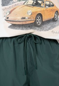 Chemise beige avec graphique de voiture de sport classique orange, associée à un pantalon à cordon vert foncé.