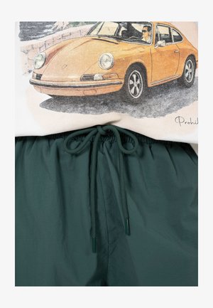 Beige paita, jossa oranssi klassisen urheiluauton grafiikka, yhdistetty tummanvihreisiin nyörillä kiristyviin housuihin.