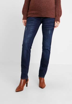 Úzké tmavě modré džíny s vybledlými detaily, spárované s hnědými vysokými botami na kotníky. Materiál vypadá jako denim s jemnou strukturou.