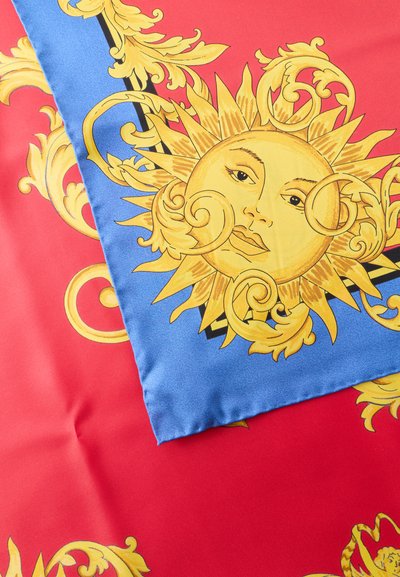 Ηλιακό πρόσωπο με στροβιλισμένες ακτίνες σε χρυσό πάνω σε μπλε ύφασμα τοποθετημένο πάνω σε κόκκινο ύφασμα με αντίστοιχα χρυσά μπαρόκ σχέδια με ρόμβους.