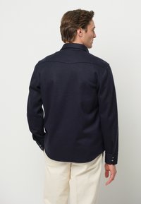 Camicia blu navy con bottoni, colletto, dettaglio sulla spalla, maniche lunghe e orlo arrotondato, realizzata in tessuto morbido.