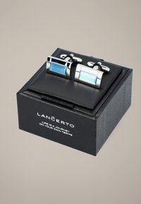 Srebrne spinki do mankietów z prostokątnymi niebieskimi wkładkami szklanymi, prezentowane w czarnym pudełku o gładkiej fakturze i prostej nadrukowanej logo.