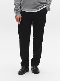 Zwarte broek met een rechte snit, gemaakt van gladde stof, gecombineerd met zwarte veterschoenen. De persoon draagt een grijs shirt met lange mouwen.