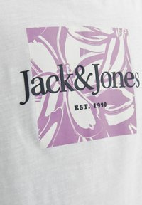 Biela tričká s fialovým grafickým dizajnom v štvorci. "Jack & Jones" a "EST. 1990" vytlačené tučným čiernym písmom.