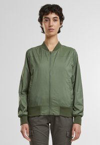 Olivovo zelená bomber bunda vyrobená z hladkého, ľahkého materiálu. Má zipsové zapínanie, rebrovaný golier a manžety, s bočnými vreckami.