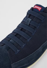 Tmavě modré tenisky s texturovaným textilním svrškem, semišovými detaily a plochými tkaničkami. Na jazyku se nachází červené a modré logo "Camper".