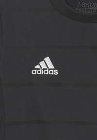 Camiseta deportiva negra con textura de rayas horizontales, cuello redondo y un logotipo bordado en blanco de Adidas en el lado izquierdo del pecho.