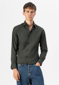 Mørkegrønn skjorte med knappestolpe, glatt tekstur, lange ermer og tettsittende design, kombinert med lyseblå denimjeans.