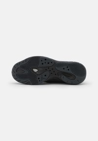 Suola di scarpa atletica nera con gomma tessurizzata, motivo a zig-zag, numerosi fori per l'aria e dettaglio del logo sul tallone.
