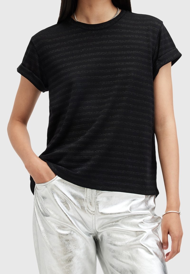 Camiseta negra de manga corta con sutil textura a rayas; Corte relajado, escote redondo, combinada con pantalones metálicos plateados brillantes.