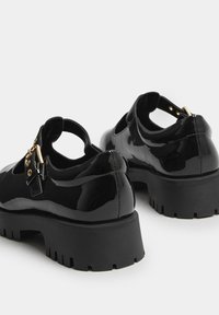 Czarne lakierowane buty na chunky podeszwie, z wycięciami i paskiem w kostce z złotą klamrą. Teksturowana gumowa podeszwa.