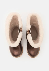 Bottes en cuir marron jusqu'à la cheville avec doublure blanche duveteuse, bout rond et boucles décoratives sur les côtés. Intérieur doux et texturé.