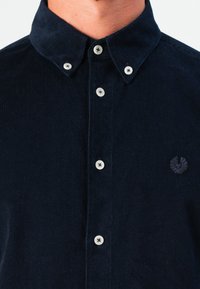 Cămașă din corduroy bleumarin cu guler butonat, prezentând nasturi albi, material texturat și un mic logo brodat pe piept.