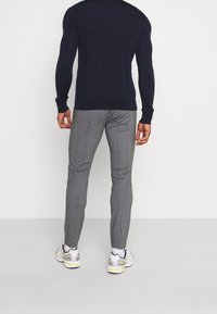 Pull en tricot bleu marine et pantalon à carreaux gris. Le pantalon est ajusté et présente un motif de checks subtil. Baskets blanches avec des accents gris.