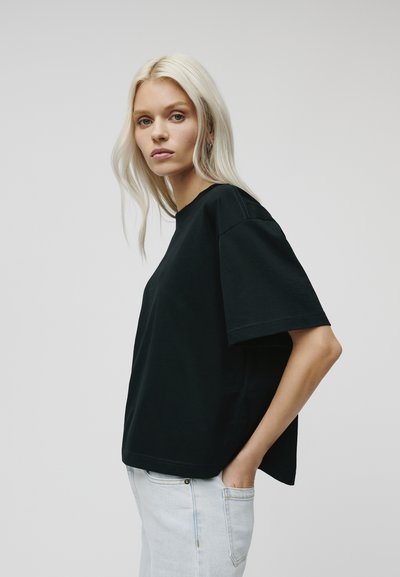 Black oversized cotton t-shirt with short sleeves, crew neck, and a relaxed fit, paired with light blue jeans. Simple, solid design.