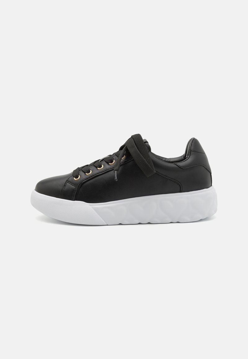 Black leather sneakers with a rounded white sole, featuring gold eyelets and black laces. Smooth texture and minimalist design.