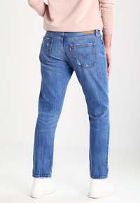 Modré džínové kalhoty s rovnými nohavicemi, mají zadní kapsy a lehké opotřebení. Oblečeno s lehkým svetr a bílými teniskami.