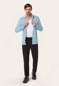 Lichtblauwe overhemd met lange mouwen over een wit t-shirt, gecombineerd met zwarte broek en zwarte schoenen. Glad materiaal en op maat gemaakte pasvorm.