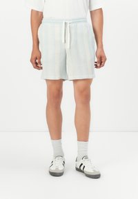 Pantalones cortos a cuadros en azul claro, confeccionados en una tela texturizada, con una cintura elástica y cordón ajustable, complementados con zapatillas blancas y calcetines grises.