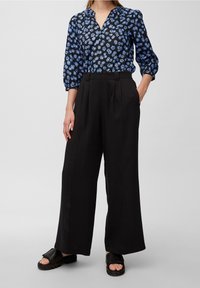 Blusa blu con motivo floreale, scollatura a V e maniche arricciate, abbinata a pantaloni neri a vita alta a gamba larga. Sandali neri scivolati.