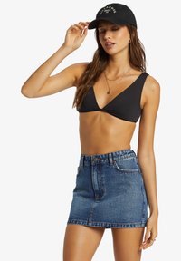 Černý bikinový top s širokými ramínky, spojený s světle modrou denimovou minisukní se zapínáním na knoflíky a zip. Černá kšiltovka doplňuje celý vzhled.
