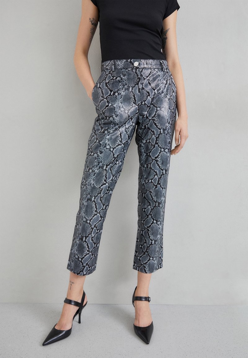 Slangenpatroon broeken in grijstinten met een strakke, gladde textuur, voorzien van een fitted taille en cropped lengte, gecombineerd met zwarte hakken.