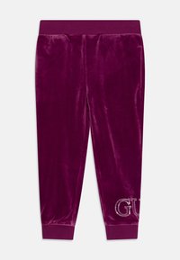 Joggers in velluto di un profondo viola con una cintura elastica. Presentano il logo luccicante "GU" sulla parte inferiore della gamba destra. Texture liscia in tutto il capo.