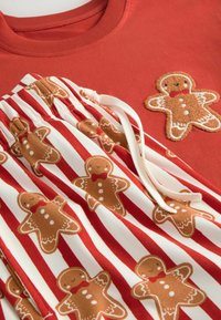 Red sweatshirt with gingerbread man applique; striped pajama pants featuring gingerbread patterns in brown and white. Soft cotton fabric.