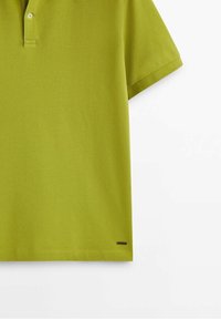 Polo vert citron à manches courtes avec deux boutons blancs et une petite étiquette noire près de l'ourlet sur le côté gauche.