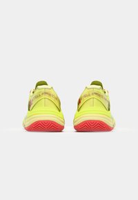 Athletic shoes featuring a bright yellow upper, green accents, and a textured red sole. Notable for their rear branding detail and unique shape.