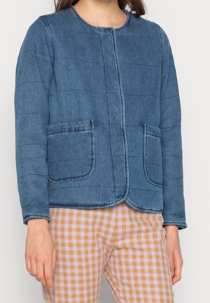 Chaqueta de mezclilla acolchada en azul medio con cuello redondo, bolsillos frontales y un corte holgado. Combinada con pantalones de cuadros claros.
