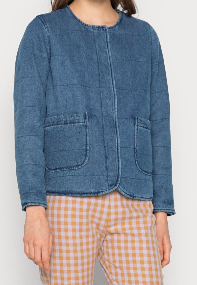 Quiltad jeansjacka i medelblått med rund halsringning, framfickor och en avslappnad passform. Matchad med ljusa rutiga byxor.