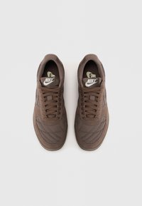 Tenisi maro Nike cu textura matlasata, accente din plasa, sireturi rotunde si talpa din cauciuc ranforsata. Logo-ul Nike este vizibil pe limba.