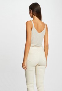 Haut sans manches beige avec un dos en V, associé à un pantalon skinny crème taille haute avec poches arrière et une texture lisse.