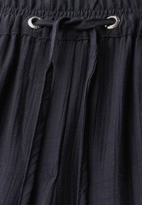 Navyblauwe geplooide stof met een elastische tailleband en een zilveren oogje voor een trekkoord. Zachte textuur, gladde afwerking.