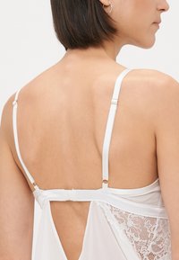 Lenjerie albă cu curele subțiri, un accent din dantelă pe spate și o bandă din satin. Țesătura pare moale și ușoară.